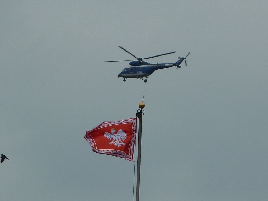 A police helicopter flies above the Royal Castle and a flag with the Polish white eagle emblem.