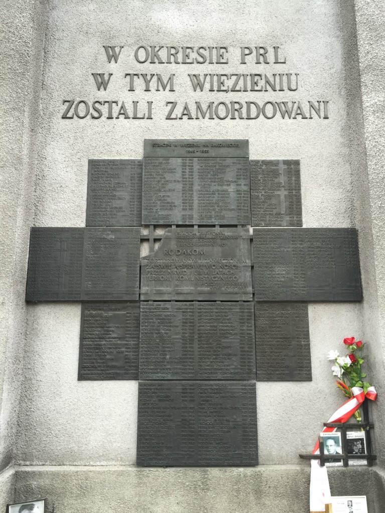 The memorial reads "During the Polish People's Republic (PRL) in this prison they were murdered." (Followed by a list of the victims)